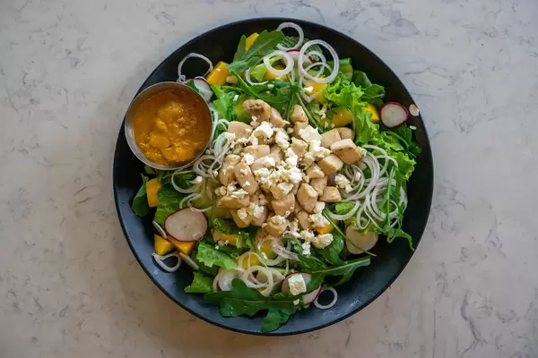 Top View Food Photo of Curry Mango Chicken Salad with Arugula, Feta Cheese and Onions on a Plate at a Restaurant