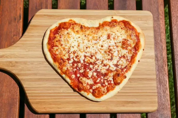 Top View Food Photo of Fresh Heart Shaped Pizza with Tomato Sauce and Cheese on a Wooden Cutting Board