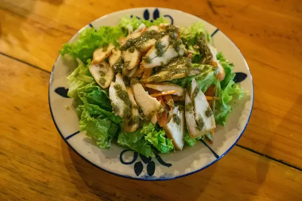 Top View Food Photo of Grilled Chicken Salad with Carrots and Dressing on a Plate in a Restaurant