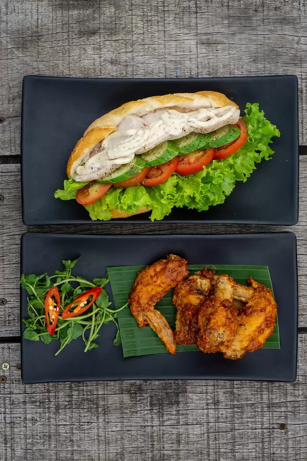Top View Food Photo of Grilled Chicken Sandwich with Cucumber, Tomato and Lettuce and Spicy Buffalo Chicken Wings on a Wooden Table