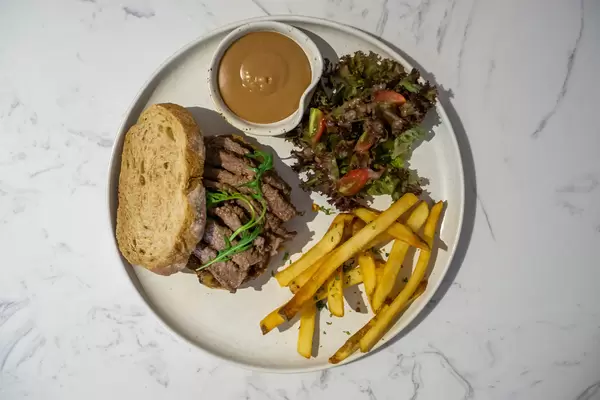 Top View Food Photo of Steak Sandwich with Salad, French Fries and Dip on a White Plate in a Restaurant