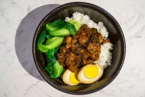 Top View Food Photo of Taiwanese Rice Bowl with Braised Pork, Duck Egg, Bok Choy and White Rice in a Black Ceramic Bowl