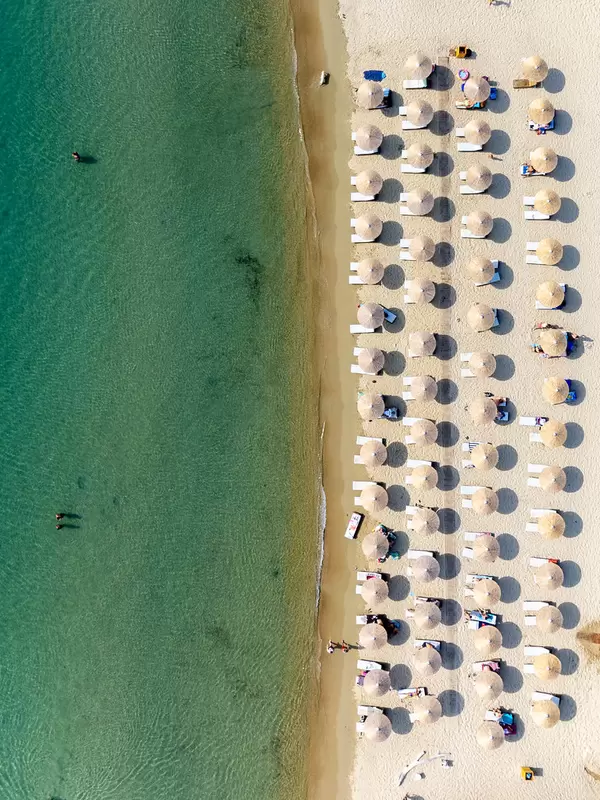 Top view: four rows of parasols on fine white sand beach with turquoise waters on Tsoungria, Greece