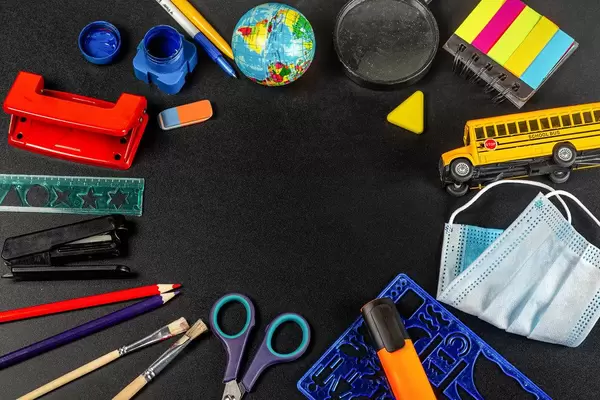 Top view, frame of school supplies with a medical mask on a black background