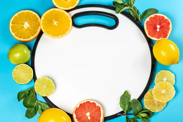 Top view, frame with fresh citrus fruits with mint on blue background with white kitchen board in the middle