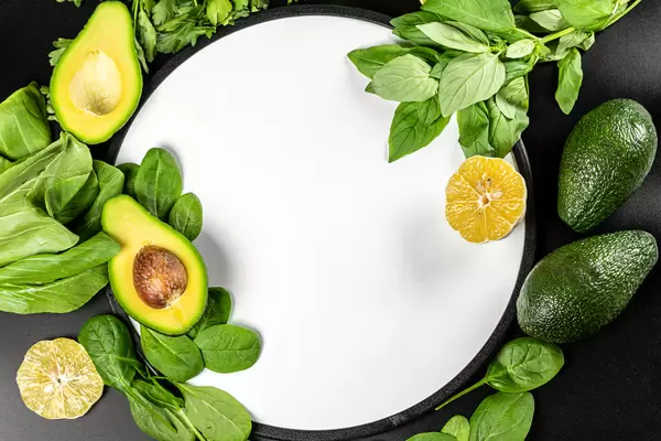 Top view, frame with green vegetables and herbs on black background with white kitchen board in the middle