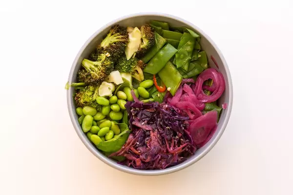 Top View Fresh Eden Bowl mit Zuckerschoten, Edamame, Spinatsalat, gerösteter Brokkoli, Ruccola, eingelegte Zwiebeln, Sesam-Rohkostsalat, Koriander ohne Sesam-Ingwer Dressing