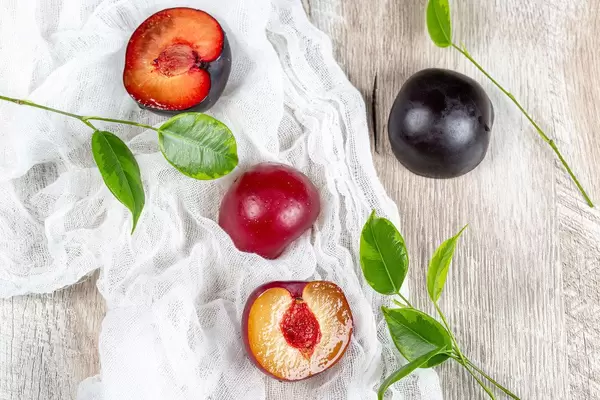 Top view, fresh plums with leaves on a grey wooden background
