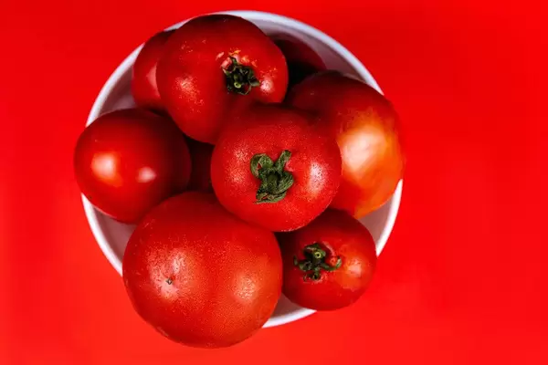 Top view, fresh red tomatoes in a bowl on a red background