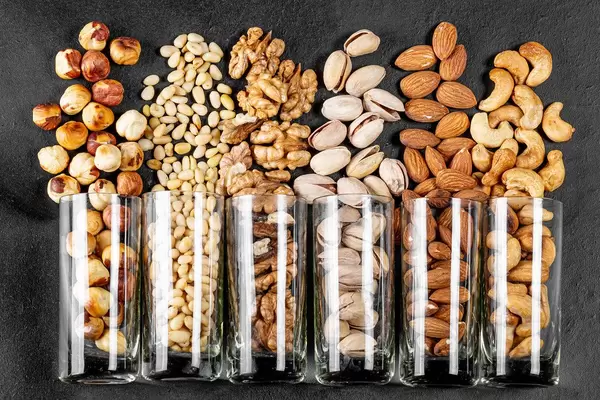 Top view, glasses with pistachios, almonds, cashews, walnuts, pine nuts and hazelnuts on a black background (Flip 2020)