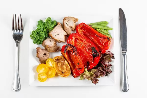 Top view, grilled meat with vegetables on a white background with a knife and fork