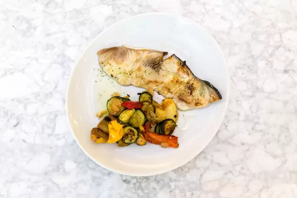 Top View - Grilled swordfish with vegetables on a white plate on granit background