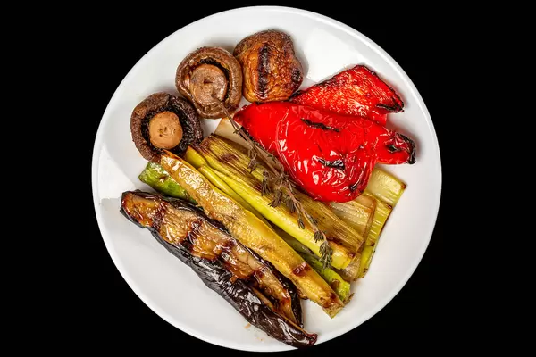 Top view, grilled vegetables and mushrooms on white plate, black background