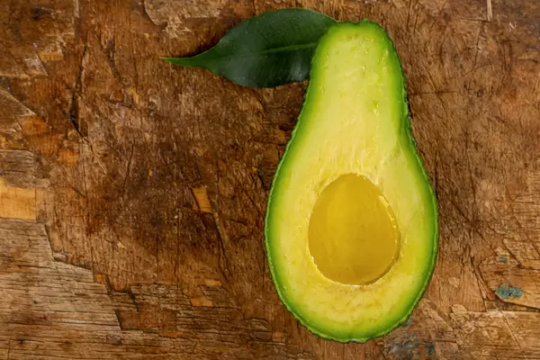 Top view, half a ripe avocado with oil and green leaf on an old wooden background