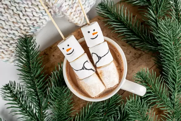 Top view, marshmallow snowmen in a cup of cocoa with branches of a christmas tree