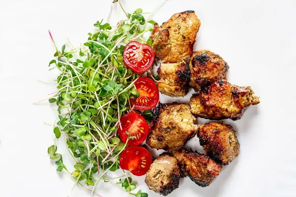 Top view meat kebab with micro-green radish and tomato slices on a white plate (Flip 2019)