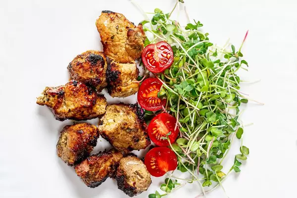 Top view meat kebab with micro-green radish and tomato slices on a white plate