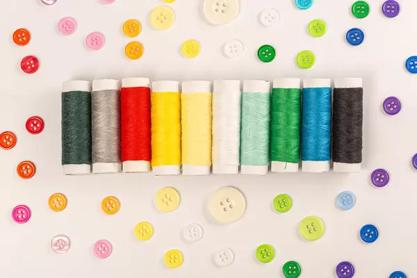 Top view, multicolored threads and buttons on white background