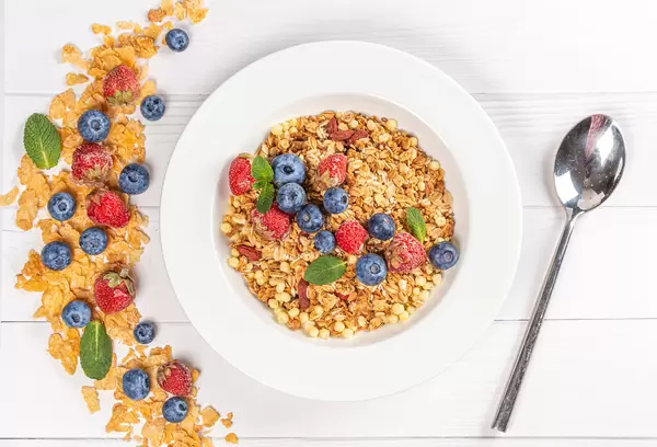 Top view, multigrain breakfast on wooden white background with strawberries, blueberries and mint leaves