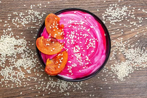 Top view-oatmeal with pink yogurt, sesame seeds and pieces of persimmon on a brown background