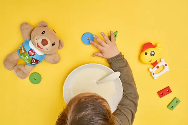 Top view of a baby boy playing with toys and eating porridge