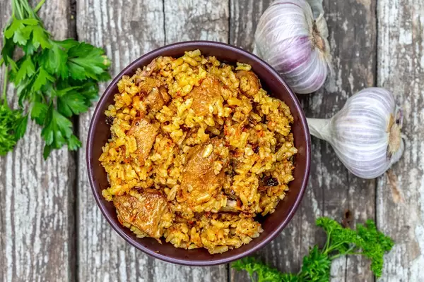 Top view of a bowl of meat pilaf on a wooden gray background with fresh parsley and garlic (Flip 2019)