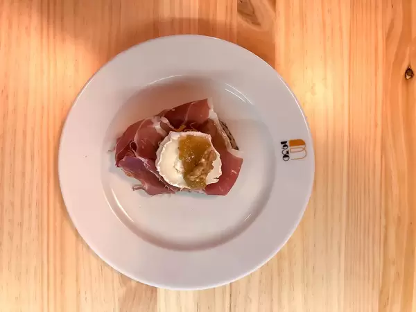 Top view of a bread snack with serano ham, soft cheese, jam and a walnut on a white plate
