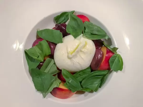 Top view of a burrata with marinated tomatoes, peaches, Kalamata olives and basil