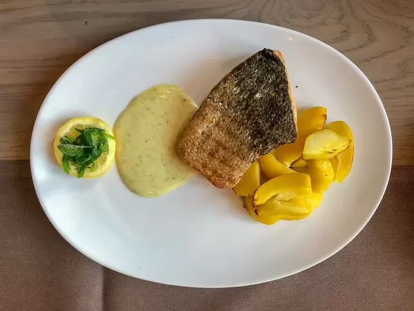 Top View of a grilled salmon fish fillet with herb dip, potato wedges and a lemon slice