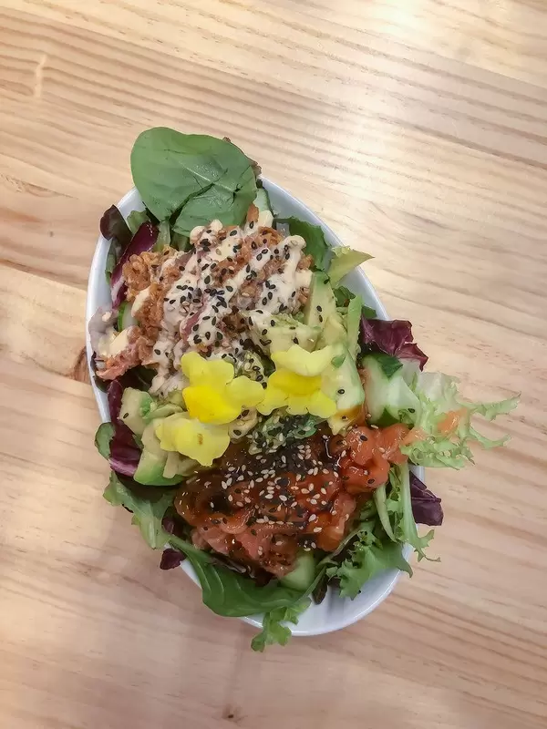 Top View of a salad made from baby-spinach, rocket, tomatoes, avocado, flowers and sesame-seeds in an oval bowl