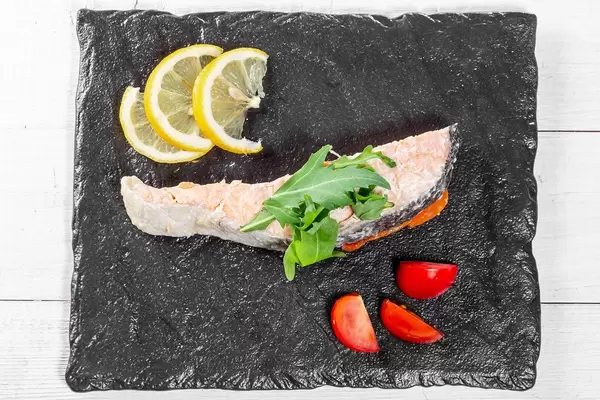Top view of baked salmon with fresh arugula, lemon and tomatoes
