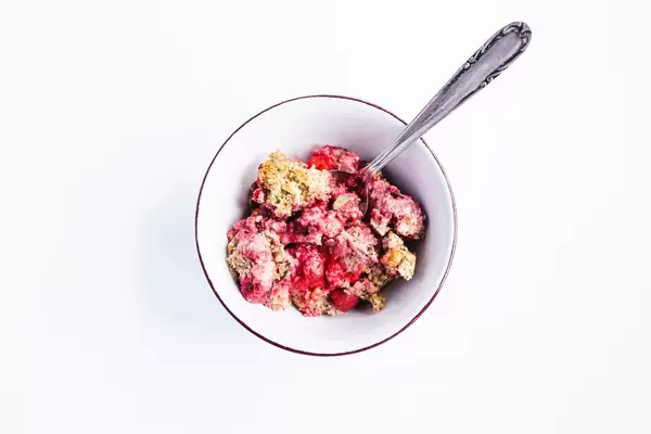 Top view of baked strawberry walnuts oatmeal in a bowl with spoon on white background