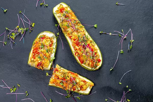 Top view of baked zucchini with vegetables and couscous on a black background with fresh micro-greens of cabbage (Flip 2019)