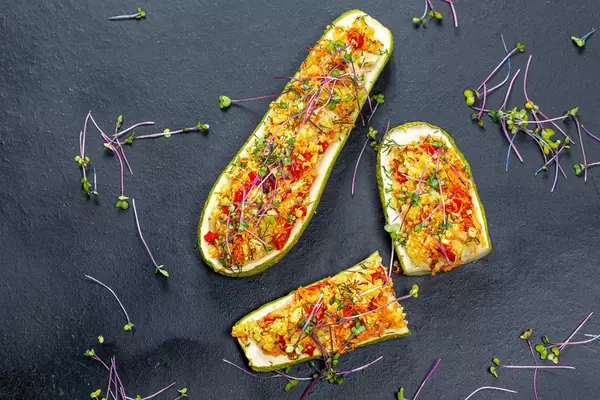 Top view of baked zucchini with vegetables and couscous on a black background with fresh micro-greens of cabbage