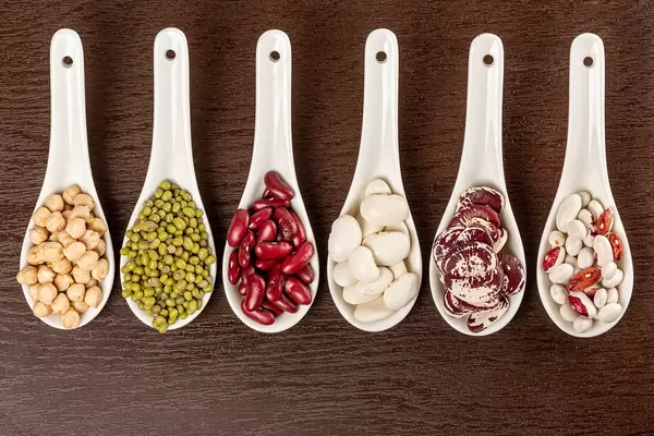 Top view of beans, chickpeas and mung in white spoons on brown background
