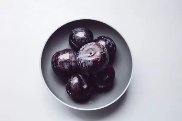 Top view of blue plums in a grey bowl. White background.