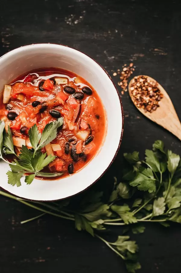 Top view of bowl of black bean chili with wooden spoon and fresh parsley