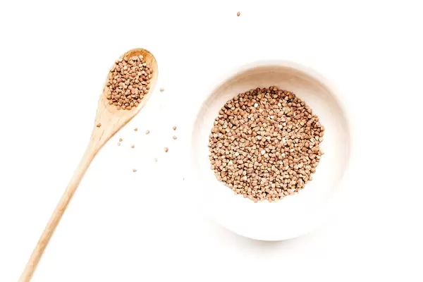 Top view of bowl of raw buckwheat groats wih wooden spoon