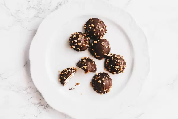 Top view of chocolate candy with nuts on top in white plate. Marbled background