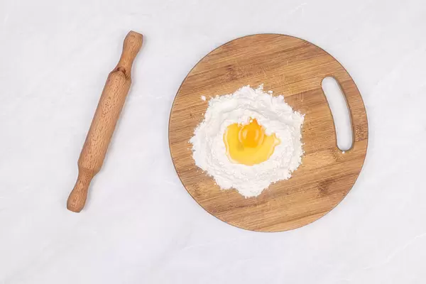 Top view of Egg on the top of the flour with wooden rolling pin