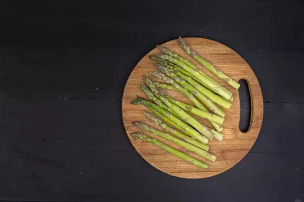 Top view of Fresh Asparagus on the round wooden board with black background with copy space