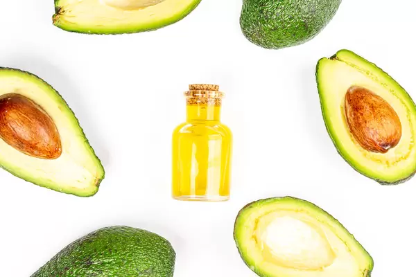 Top view of fresh avocado frame and bottle with oil on white background