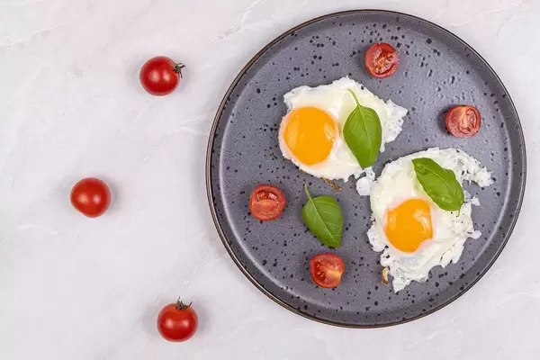 Top view of Fried Eggs served with Cherry tomatoes and Basil