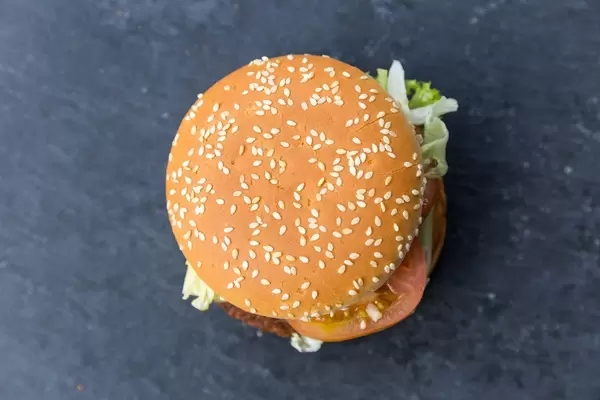 Top view of German McDonalds Burger and meat substitute "Big Vegan TS" with soy patty, leaf salad and vegetables in sesames bread on a dark surface