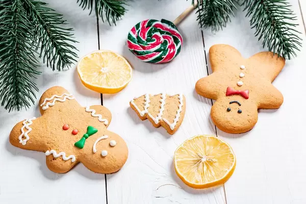 Top View of gingerbread men next to Lemon Slices, Lollipop and Tree Branches on a white wooden Table