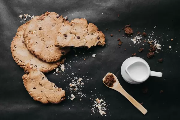 Top view of homemade chocolate cookies, dark brown sugar and milk on dark background. Food styling.