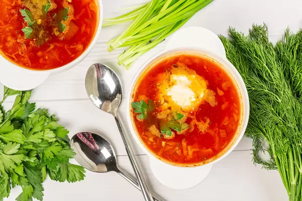 Top view of hot beetroot soup with sour cream and fresh parsley, dill and green onions