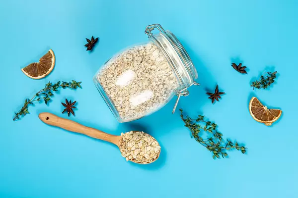 Top view of jar and wooden spoon with oatmeal on blue background with thyme, star anise, dried orange