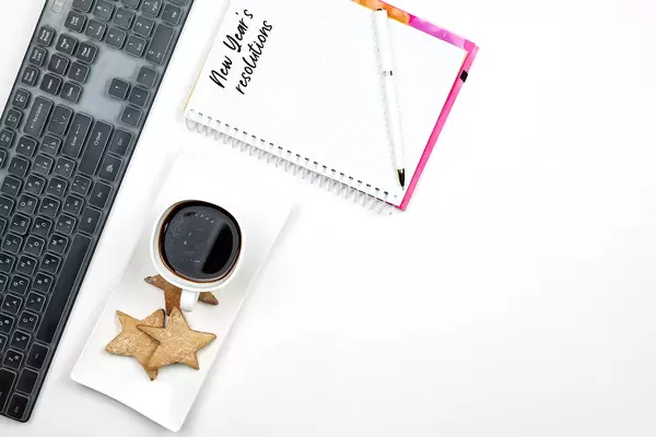 Top view of notepad with a phrase - New year resolutions over pc keyboard, a cup of coffee and cookies