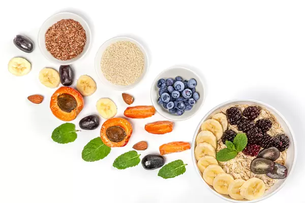Top view of oatmeal, fruits, seeds and mint leaves on white